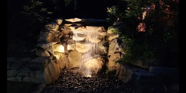 Illuminated stone cave entrance at night with warm lighting, surrounded by dark trees and rocky terrain