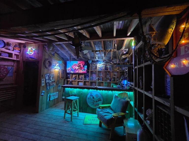 Neon-lit bar interior with turquoise glowing counter, colorful signs, and dark exposed ceiling beams