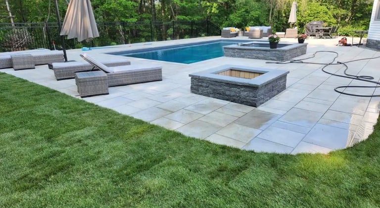 Luxury backyard with rectangular swimming pool, gray lounge chairs, stone fire pit, and patio surrounded by green lawn and trees